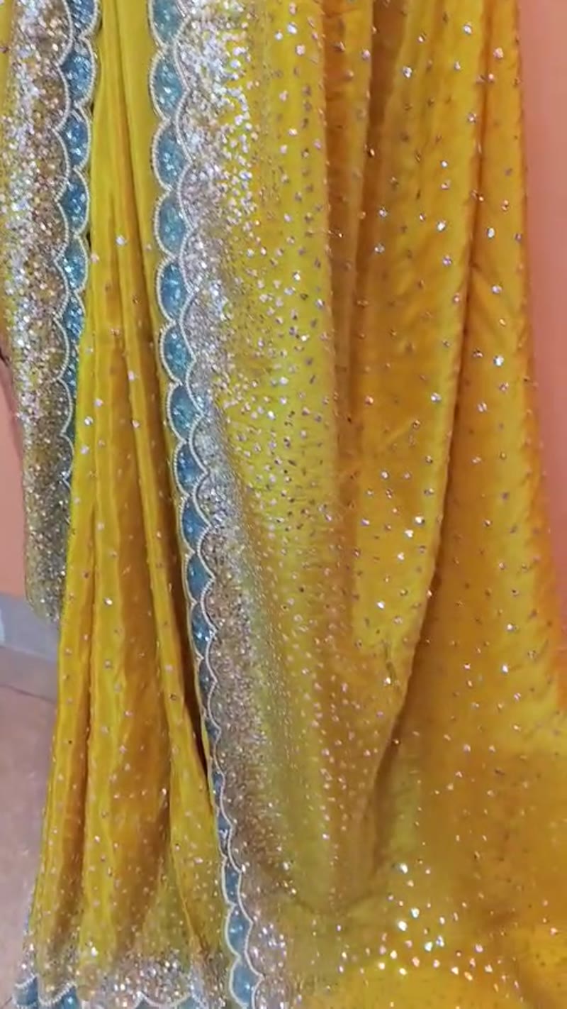 A yellow georgette saree with a scalloped stone-work border, shown in the showroom